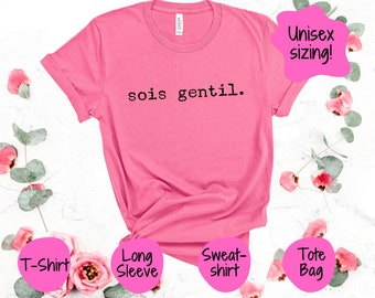 May include: Pink t-shirt with the text "sois gentil." in black typewriter font. The shirt is available in a variety of styles, including a long-sleeve t-shirt, a sweatshirt, and a tote bag. The text "Unisex sizing!" is in a pink speech bubble.