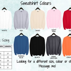 May include: A chart showing sweatshirt colors and unisex sizing. The colors are white, ash, sand, light pink, red, indigo blue, black, dark heather, and orange. The sizing chart shows sizes S, M, L, XL, and 2XL with corresponding width and length measurements in inches.