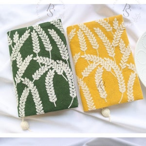 May include: Two book covers with a white floral design on a green and yellow background. The covers have a white tassel.