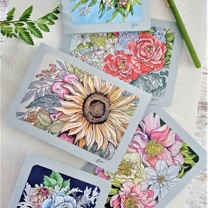 May include: Four greeting cards with floral illustrations. Each card features a different bouquet of flowers, including sunflowers, roses, and peonies. The cards are all on a light blue background with a white border.