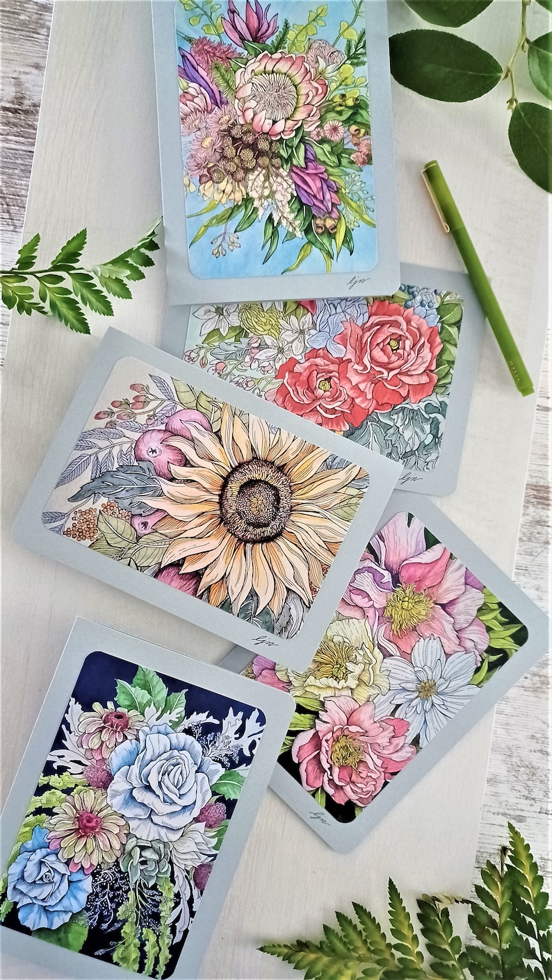 May include: Four greeting cards with floral illustrations. Each card features a different bouquet of flowers, including sunflowers, roses, and peonies. The cards are all on a light blue background with a white border.