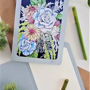 May include: A greeting card with a blue, white, and pink floral bouquet illustration on a dark blue background. The card is folded in half and has a blank inside for writing a message.