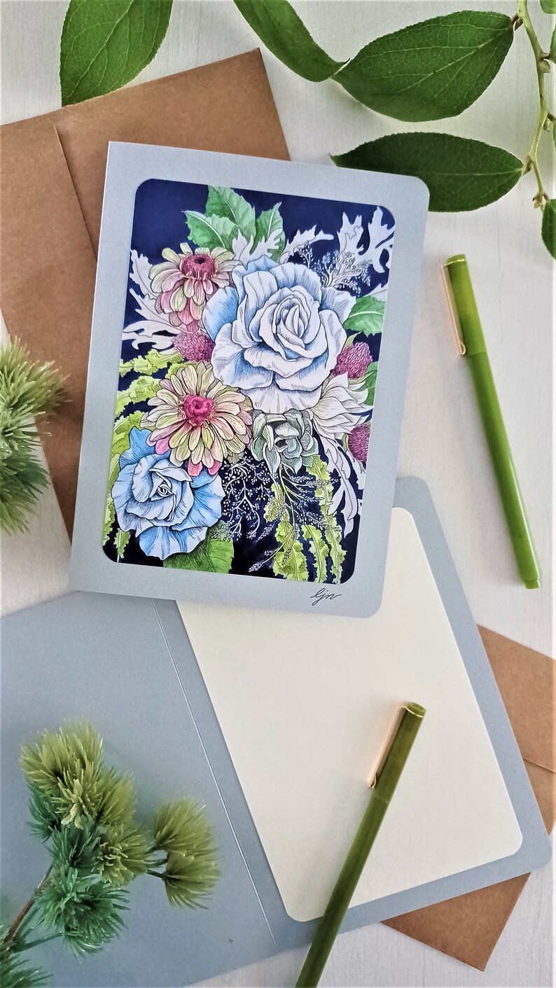 May include: A greeting card with a blue, white, and pink floral bouquet illustration on a dark blue background. The card is folded in half and has a blank inside for writing a message.