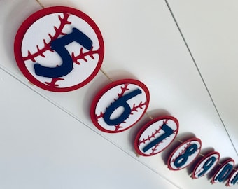 May include: A baseball-themed banner with red and white baseballs and black numbers 5 through 11. The banner is strung together with twine.
