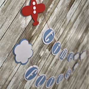 May include: A blue and white paper banner with the words "Time Flies" and clouds hanging from a red airplane cutout.