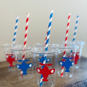 May include: Six clear plastic cups with red and blue striped straws. Each cup has a red or blue airplane sticker with white stars.