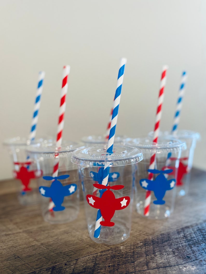 May include: Six clear plastic cups with red and blue striped straws. Each cup has a red or blue airplane sticker with white stars.
