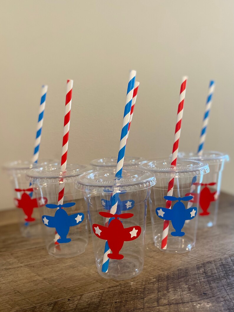 May include: Six clear plastic cups with red and blue striped straws. Each cup has a red or blue airplane sticker with white stars on it.