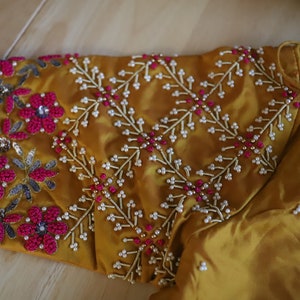May include: A mustard yellow fabric with intricate embroidery featuring pink and white beads, sequins, and floral designs.