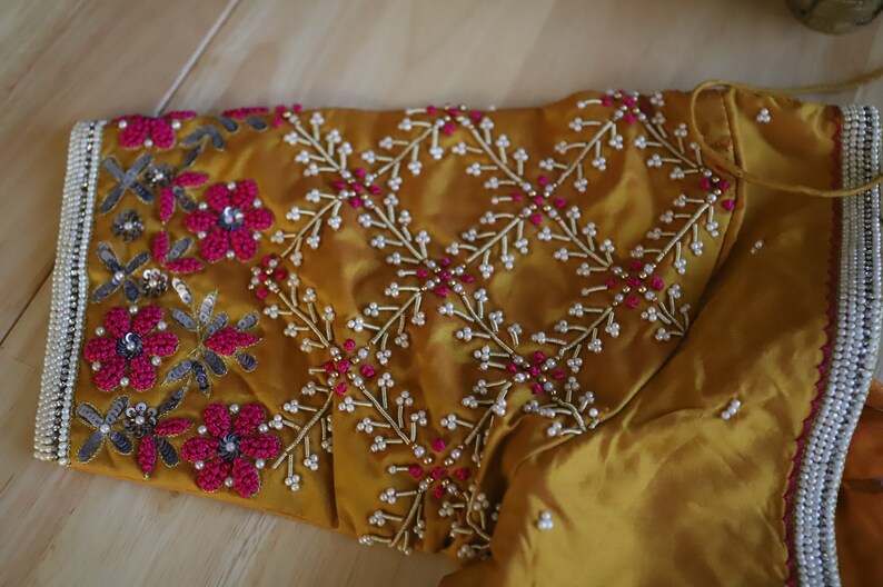 May include: A mustard yellow fabric with intricate embroidery featuring pink and white beads, sequins, and floral designs.