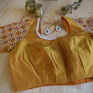 May include: A mustard yellow embroidered blouse with a white trim and pink and silver embellishments.
