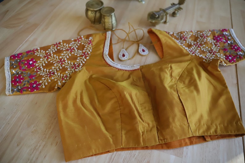 May include: A mustard yellow embroidered blouse with a white trim and pink and silver embellishments.