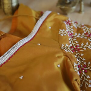 May include: A mustard yellow fabric with a white and pink beaded design. The fabric has a beaded trim around the neckline.