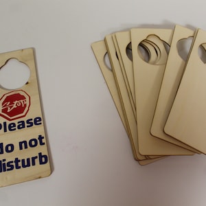 May include: A stack of blank wooden door hangers with a single door hanger with the text "Please do not disturb" and a red stop sign with a diagonal line through it.