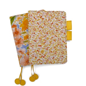 May include: Two rectangular planner covers featuring floral patterns. The front cover has a dense print of small orange and pink berries on a white background, while the partially visible back cover displays larger orange and pink watercolor flowers.