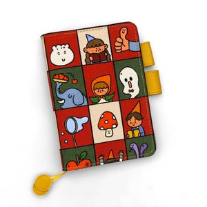 May include: A rectangular notebook cover featuring a grid of colorful cartoon illustrations including a ghost, an elephant, a mushroom, and a person reading. The cover has a red and green background with yellow pen loops and a yellow circular zipper pull.