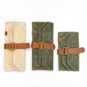 Könnte beinhalten: Drei Leinwand-Rolletuis in Creme, Olivgrün und Dunkelgrün. Jedes Etui hat einen braunen Lederriemen mit einer Messingschnalle. Die Etuis sind mit dem Markennamen "Natsume" und "The Curated" versehen.