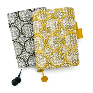 May include: Two rectangular notebook covers featuring a floral pattern with a grid of raised dots. One cover is white with olive green flowers and dark green dots, while the other is white with yellow flowers and bright yellow dots.