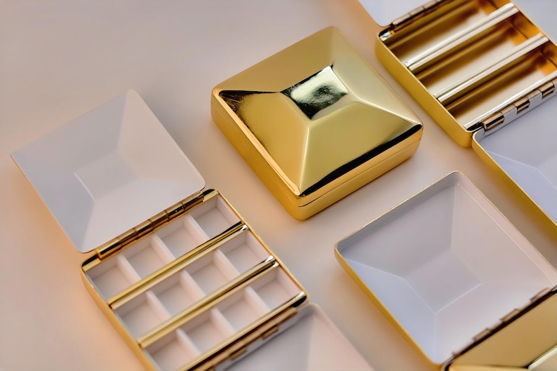 Puede incluir: Cajas de joyer&iacute;a geom&eacute;tricas doradas con interiores blancos. Algunas cajas est&aacute;n abiertas, revelando compartimentos y divisores. Las cajas tienen una superficie brillante y reflectante, y las tapas est&aacute;n articuladas. El dise&ntilde;o general es moderno y elegante.