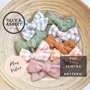 Peut inclure: Un ensemble de huit nœuds en tissu pour cheveux dans différentes couleurs et motifs, y compris du vichy, uni et imprimé animal. Les nœuds sont disposés dans un bol en bois. Le texte "Tilly & Ashley Est. 2020" et "Plus Video" est visible sur l'image. Le texte "PDF Sewing Pattern" est également visible sur l'image.