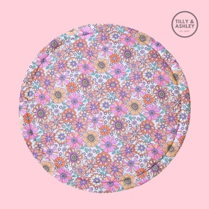 May include: A round, floral-patterned mat featuring a repeating design of pink, orange, and purple flowers on a white background. The mat has a quilted edge and the text "Tilly & Ashley Est. 2020" in a circle.