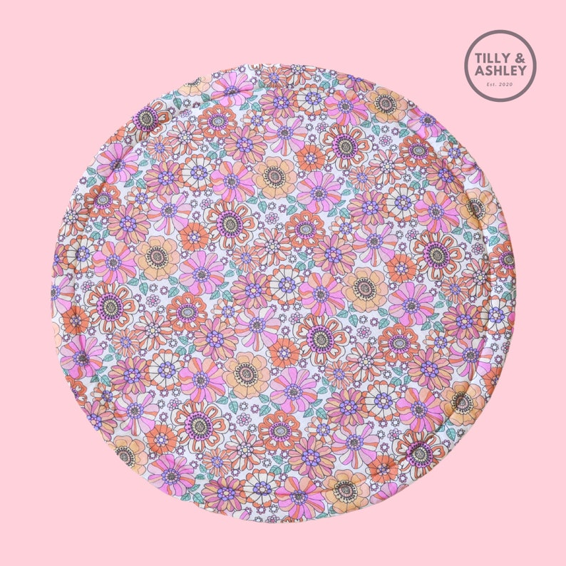 May include: A round, floral-patterned mat featuring a repeating design of pink, orange, and purple flowers on a white background. The mat has a quilted edge and the text "Tilly & Ashley Est. 2020" in a circle.