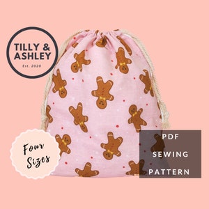 May include: A pink drawstring bag with a gingerbread man pattern. The bag has a white drawstring and the text "TILLY & ASHLEY Est. 2020" and "Four Sizes" on it. The bag is a PDF sewing pattern.