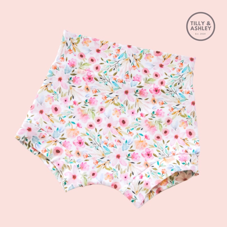 May include: White cotton baby bloomers with a pink and green floral print. The print features watercolor-style flowers and leaves.
