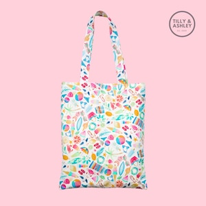May include: White tote bag with a colorful summer-themed print featuring various beach items like flip flops, ice cream cones, watermelon slices, and palm trees. The bag has two handles and the text "TILLY & ASHLEY Est. 2019" is printed on a small circle in the top right corner.