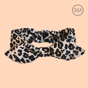 Puede incluir: Una diadema de leopardo blanca, negra y rosa con un lazo anudado.