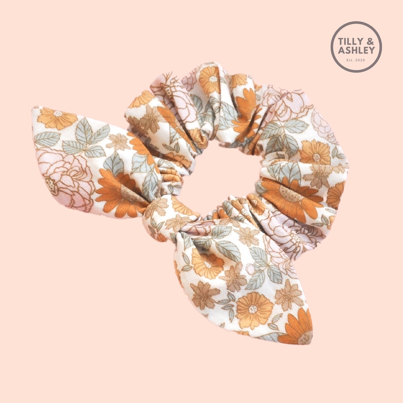 May include: A white and brown floral patterned scrunchie with a bow. The scrunchie is made of fabric and has a gathered look.