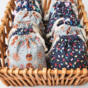 May include: A wicker basket filled with small fabric gift bags. The bags have different Christmas-themed patterns, including gingerbread men, candy canes, and Christmas lights.
