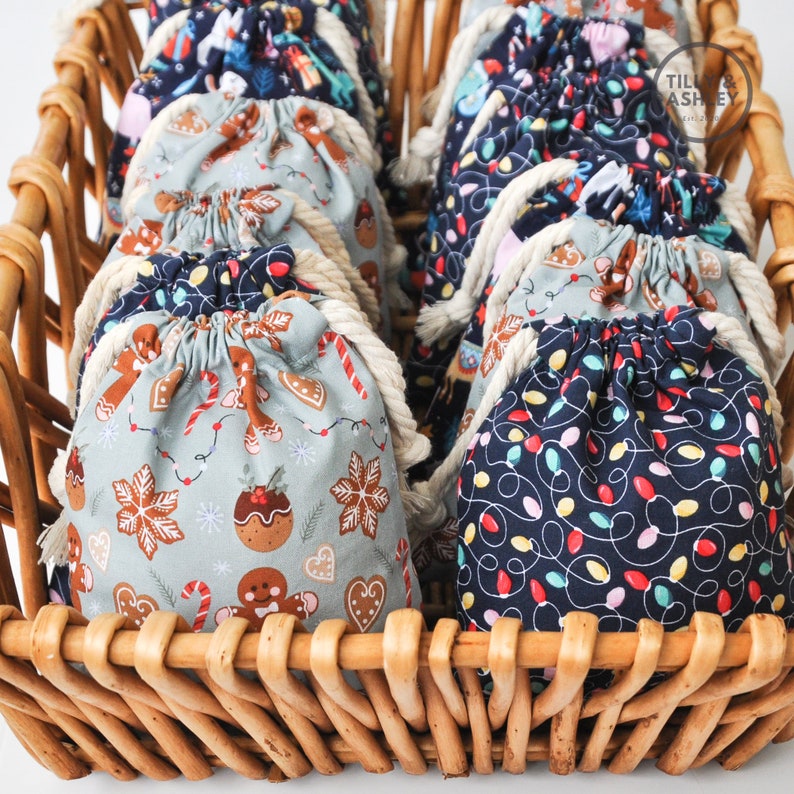 May include: A wicker basket filled with small fabric gift bags. The bags have different Christmas-themed patterns, including gingerbread men, candy canes, and Christmas lights.