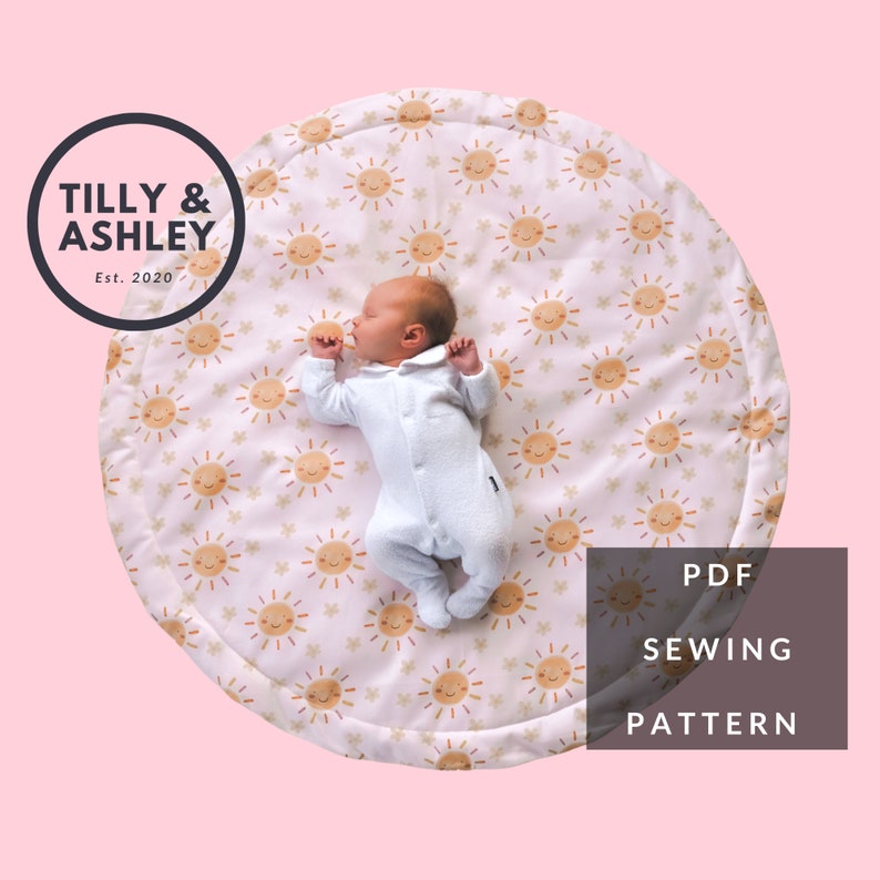 May include: A baby lies on a round play mat with a repeating pattern of smiling suns and stars. The mat is white with a pinkish hue. The text "PDF SEWING PATTERN" is in a brown rectangle. The Tilly & Ashley logo is in a black circle.