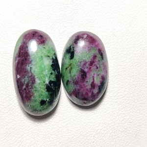 Könnte beinhalten: Zwei ovale, grüne, rosafarbene und schwarze Edelsteine. Die Edelsteine sind glatt und poliert.