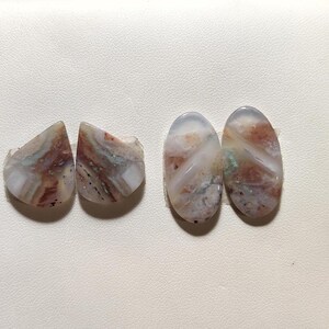 May include: Four polished gemstones in shades of white, brown, red, and green. Two are oval, two are triangular. The stones have a natural, earthy appearance. The gemstones are suitable for jewellery making.