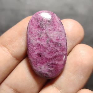 Könnte beinhalten: Ein ovaler Cabochon-Edelstein in Rosa und Weiß mit einer glatten, polierten Oberfläche.