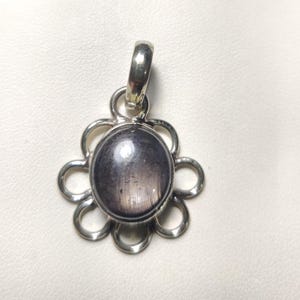 Pode incluir: Pingente de prata com uma grande pedra preciosa cinza oval no centro. A pedra preciosa é cercada por um design floral prateado. O pingente tem uma argola de prata na parte superior para uma corrente.