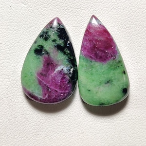Könnte beinhalten: Ein Paar tropfenförmige grüne und rosa Edelsteine mit einem schwarz-weißen Muster.