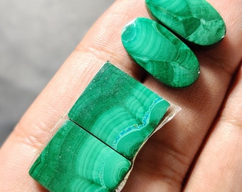 May include: Two oval-shaped green malachite cabochons and two square-shaped green malachite cabochons. The stones have a swirling pattern of green and blue.
