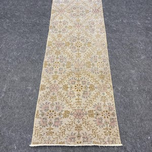 May include: A rectangular, vintage-style rug with a floral pattern in muted tones of beige, pink, and gold. The rug has a distressed look, suggesting it is an antique or a reproduction with a worn aesthetic. The rug is suitable for a hallway or entryway.