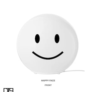 Puede incluir: Lámpara de mesa de cerámica blanca con forma de cara sonriente con contorno negro. La lámpara tiene un cable y un interruptor.