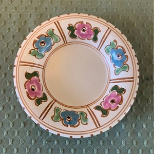 May include: A white ceramic plate with a brown rim and floral design. The flowers are pink, blue, and green.