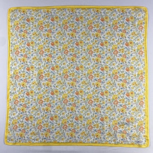 Könnte beinhalten: Quadratischer Stoff mit floralem Muster. Der Stoff hat einen weißen Hintergrund, der mit gelben, orangefarbenen und blauen Blumen bedeckt ist. Ein leuchtend gelber Rand umrahmt das florale Design. Das Wort "LIBERTY" ist unten rechts aufgedruckt.