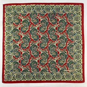 Peut inclure: Un carré de tissu rouge à motifs cachemire avec une bordure détaillée. Le tissu présente un motif répété de motifs cachemire verts, bleus et jaunes sur un fond rouge. La bordure est un motif répété de vert et de bleu.