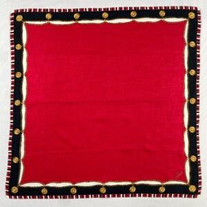 May include: Square red scarf with a black border featuring gold-coloured circular accents and a chain design. The scarf has a white and black striped edge.