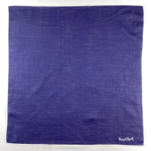 May include: A square, indigo-coloured handkerchief with a white border. The fabric has a textured appearance. The lower right corner features the white cursive text "Margaret Howell".