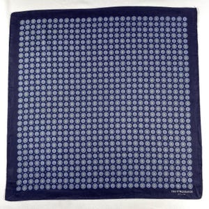 Könnte beinhalten: Marineblaues Einstecktuch mit einem sich wiederholenden Muster aus weißen und hellblauen Kreisdesigns. Das Einstecktuch hat einen dunkelblauen Rand und der Markenname "TRUSSARDI" ist in Weiß unten rechts aufgedruckt.