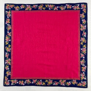 May include: A square scarf in a vivid pink hue, framed by a navy blue border. The border features a floral design in pink, yellow, and white. The central area of the scarf is a solid, bright pink.