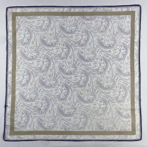 Peut inclure: Carré de mouchoir à motif cachemire. Le tissu blanc présente un motif cachemire lavande répété. Une bordure beige encadre le motif, avec une bordure bleu marine. Le nom de la marque est imprimé en bas à droite.